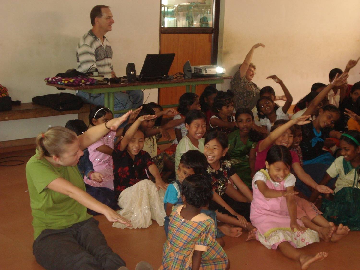 A group of people sitting on the floor with their hands up.