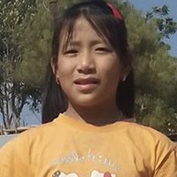 A young girl wearing an orange shirt and smiling.