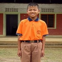 A boy in an orange shirt stands outside.