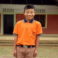 A boy in an orange shirt stands outside.