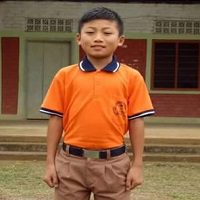 A young boy in an orange shirt stands outside.