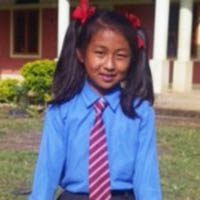 A young girl in blue shirt and tie standing outside.