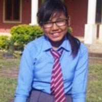 A girl in blue shirt and tie sitting on grass.