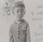 A young boy standing in front of a wall.