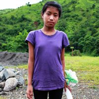 A young girl standing in the dirt near some rocks.