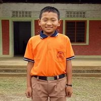 A young boy in an orange shirt stands outside.