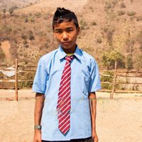 A young man wearing a tie standing in the dirt.