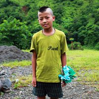 A young boy standing in the grass holding onto some trash bags.