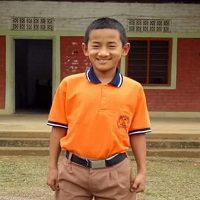 A young boy in an orange shirt stands outside.