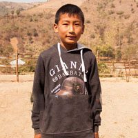 A young boy standing in front of a fence.