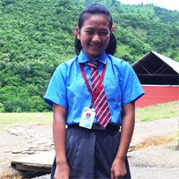 A girl in blue shirt and tie standing on dirt ground.