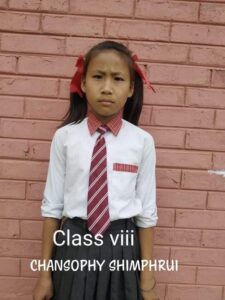 A girl in school uniform standing against a brick wall.