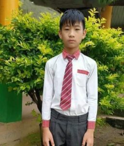 A young man in a tie and shirt standing next to bushes.