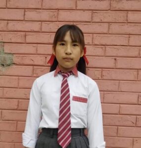 A girl in school uniform standing against a brick wall.