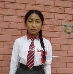 A girl in school uniform standing against a brick wall.
