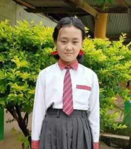 A girl in school uniform standing next to a tree.