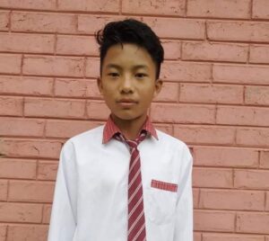 A young man wearing a red tie standing in front of a brick wall.