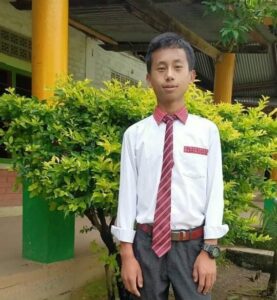 A young man in a tie standing next to a tree.