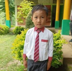 A young boy in a tie standing outside.