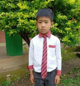 A young boy wearing a tie and standing in front of a tree.