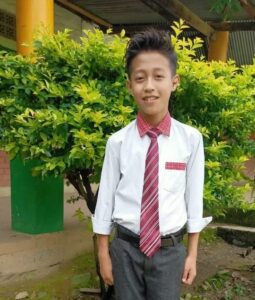 A young man in a tie standing next to a tree.