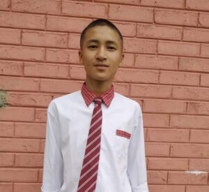 A young man wearing a red tie standing in front of a brick wall.