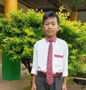 A young man in a tie standing next to a tree.