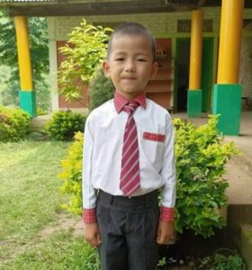 A young boy in a tie standing outside.