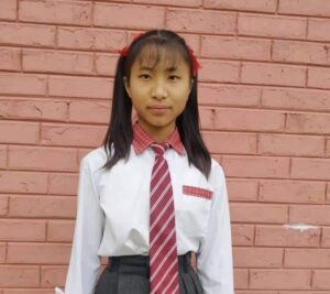 A girl in school uniform standing against a brick wall.