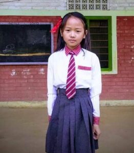 A girl in school uniform standing on the sidewalk.