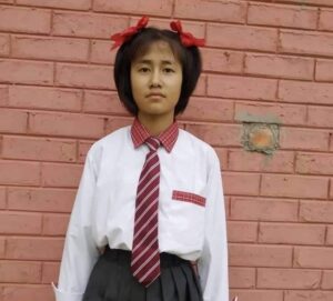 A girl in school uniform standing against a brick wall.