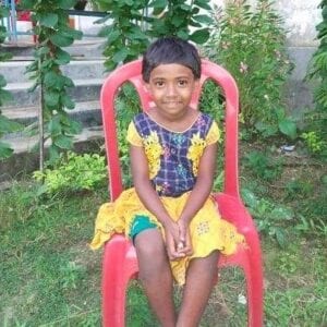 A girl sitting on a red chair in the grass.