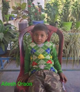A young boy sitting in a chair with plants behind him.