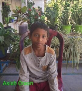 A young boy sitting in a chair with plants behind him.