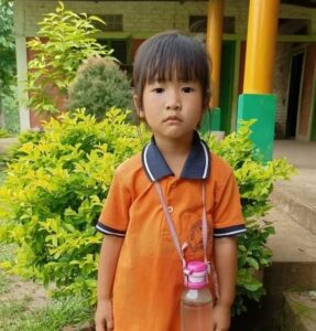 A young boy in an orange shirt and a pink cup