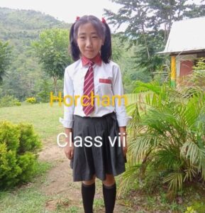 A girl in school uniform standing on the grass.