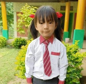 A young girl in school uniform standing outside.