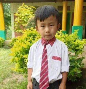 A young boy wearing a red tie and black pants.