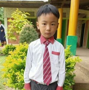 A young boy in a tie standing outside.