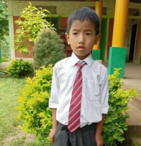 A young boy in a tie standing outside.
