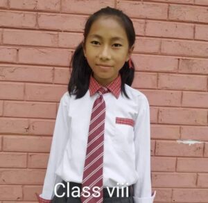 A girl in school uniform standing against a brick wall.