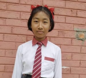 A girl in school uniform standing against a brick wall.