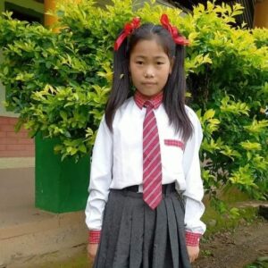 A girl in school uniform standing next to bushes.