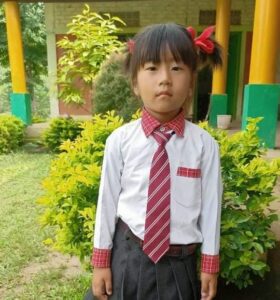 A young girl in school uniform standing outside.