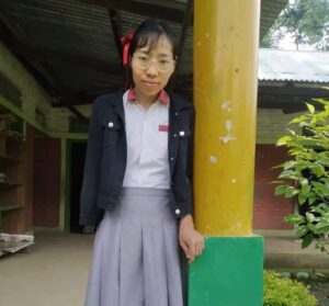 A girl standing next to a pole in front of a building.