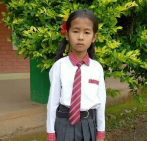 A young girl in school uniform standing next to a tree.