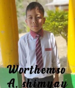 A young boy wearing a tie and standing in front of yellow pillars.