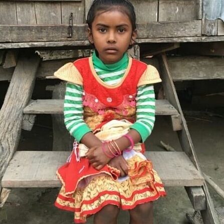 A young girl sitting on top of a wooden bench.