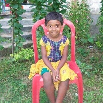 A girl sitting on a red chair in the grass.