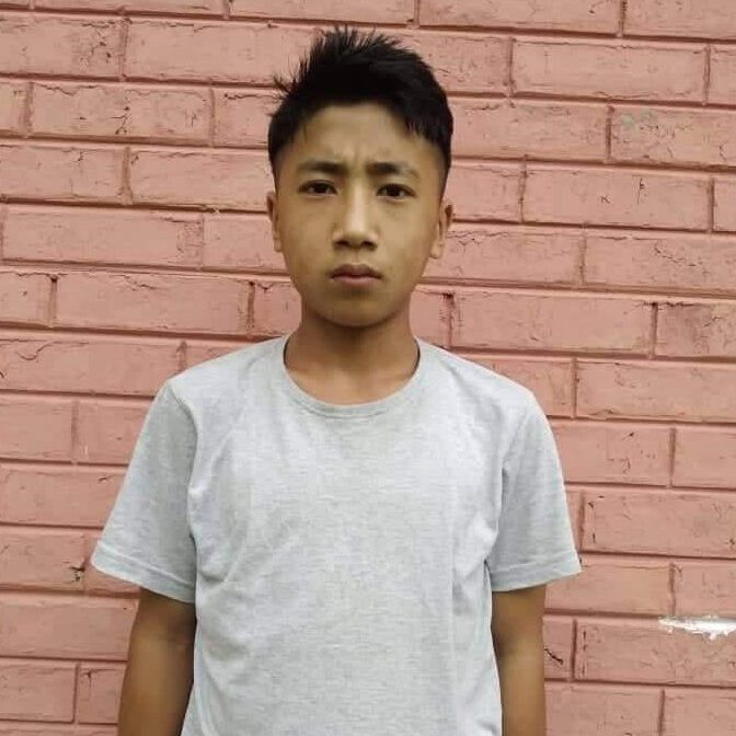 A young man standing in front of a brick wall.